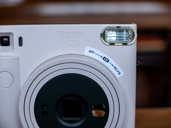 Máy ảnh lấy liền Instax Square SQ1 được bật nguồn bằng cách xoay lens từ Tắt sang Bật.